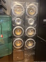 Pair of two tall floor-standing Pure Acoustics QX900F speakers wrapped in clear plastic, showing multiple yellow cone drivers and silver trim rings on black cabinet.