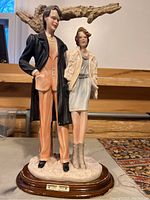 Front side view of the porcelain figurine showing man and woman standing on a white base with wooden platform beneath.