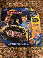 Front view of sealed Beyblade Legends Super Vortex Battle Set box showing two red and silver Beyblade tops and stadium graphic.