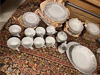 Full set arranged showing cups, saucers, plates, sugar and creamer, large bowls on patterned carpet.