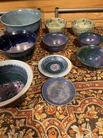 Overview of vintage pottery lot showing a variety of bowls and plates in different colors and glaze finishes placed on a patterned fabric.