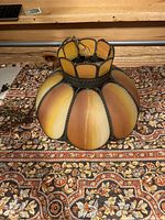 Close-up image of the slag glass lamp shade showing the amber and brown tinted glass panels with bronze brass framing and decorative beading around edges.