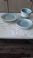 Photo showing 4 dinner plates stacked, 4 salad plates stacked, and 4 ceramic bowls stacked on a marble countertop.