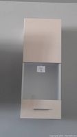 White wall mount cabinet with closed top door, open middle shelf, bottom drawer, silver handle