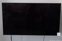 Front view of 55 in LG TV mounted on wall with power cables visible