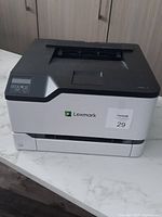 Lexmark colour laser printer on table showing top and front panel with logo and control buttons.