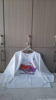 Full view of the white NHL Power Play jersey on a hanger, showing the front logo and overall condition.