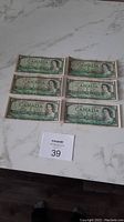 Six Canadian one dollar bills placed side by side on a marble surface.