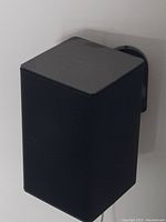 Black cube speaker mounted on wall bracket with grille front