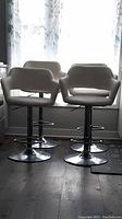 Four off-white leather stools grouped in front of window showing overall set