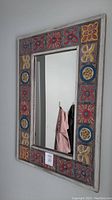 Rectangular decorative wall mirror with multicolor hand-painted tile frame, hung on a gray wall.