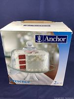 Original box showing the clear glass cake stand with dome lid containing a cake.