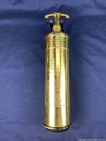 Full view of antique brass fire extinguisher showing polished finish and cylindrical shape against blue cloth background.