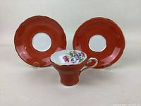 Front view of tea cup displaying floral interior and two matching orange glazed saucers with scalloped edges behind it.
