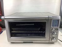 Front view of stainless steel Breville toaster oven showing the closed glass door, handle, and part of the control panel on the right.