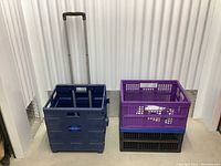 Set of three collapsible plastic baskets including navy blue basket with wheels and handle, purple basket, and black basket stacked.