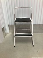Front view of the white metal 2-step ladder showing the steps and handle.