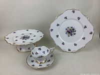 Photo showing all five pieces: tea cup, saucer, plate, and two pedestal serving dishes with Sweet Violets pattern and gold edge trim.