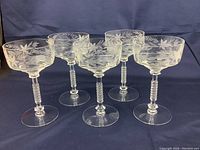 Set of 5 crystal glasses with etched leaf design and long textured stems shown from an angle.