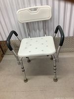 Front angle view showing full shower chair structure, white plastic seat with holes, black armrests, and aluminum frame with rubber feet.