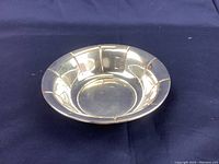 Sterling silver bowl positioned on navy blue fabric, showing angled front view highlighting depth and sectioned design.