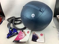 Photo showing the full set including black Ugi 12 lb exercise ball, resistance band with foam grips, mesh bag, and two Ugi instruction booklets.