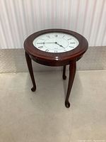 Full side view of dark brown wooden end table with built-in round clock on the top surface, showing its four curved legs.