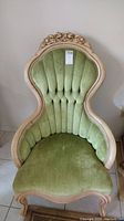 Full view of green upholstered chair with carved wood frame and floral detail