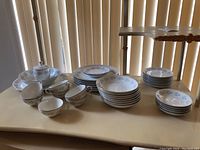Full view of all porcelain dinnerware pieces arranged on a table, showing cups, plates, bowls, and platter.