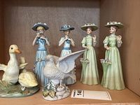 Front view of porcelain bird and lady figurines showing detailed dress and bird feathers.