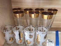 Photo of the full set of 7 beer glasses with wide gold rims and 4 water glasses with gold leaf design.