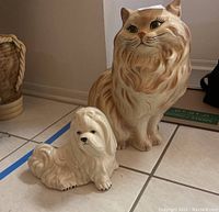 Photo of both large ceramic cat and dog figurines on a tiled floor showing size comparison and detail