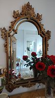 Full view of large rectangular arched wall mirror with red flowers reflected in glass and ornate gilded frame.