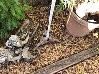 Metal tripod plant stand next to large terracotta pot and garden figurines on leaf-covered ground