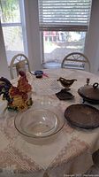 Photo of silverplate items and glassware on table including rooster canister, cut glass cake plate, glass bowl, and several silverplated serving dishes.