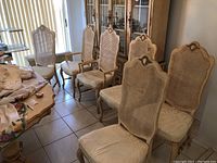 Six French Provincial dining chairs with cane backs and upholstered seats, visible in a room with tiled floor, one seat and one cane back showing damage.