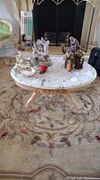 Full view of the oval living room table with marble top showing carved wooden legs and floral carpet underneath. Porcelain figurines on table are excluded.