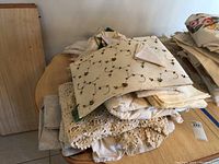 Stack of various folded vintage and crochet table linens and cloths including lace and cotton items on a table.