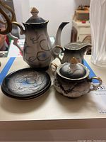 Full view of tea service set showing teapot, sugar bowl with lid, creamer, and three saucers with dragon motif and gold trim.