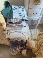Stack of towels in various colors and folded fabric with green leaf floral pattern on top, positioned on a chair.