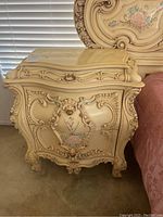 View of one bedside table showing ornate carved wooden details and floral painted front panel