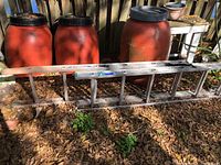 Side view photo of the Werner aluminum ladder on the ground with visible bend on the top left rail and black plastic end caps. Ladder shown fully retracted with 3 sections visible.