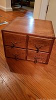Photo showing the wooden box with four drawers, unique dark decorative handles, and the general shape and finish of the box.