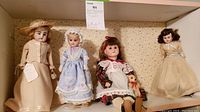 Four vintage dolls with period clothing displayed on shelf