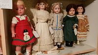 Five vintage dolls displayed together on a shelf in a row, showcasing various sizes, materials, and clothing.