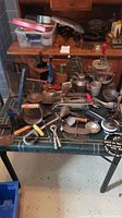 Top-down view of various antique kitchen tools arranged on a table including grinders, egg beaters, strainers and ladles.