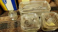 Photo showing 5 clear ribbed glass refrigerator storage jars with fitted lids and a small clear glass inkwell on a carpeted floor.