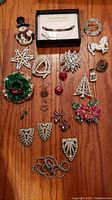 Photo showing assorted vintage costume jewelry pins and brooches laid on wooden surface. Includes Christmas themed pieces, rhinestone brooches, and enamel pins.
