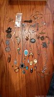 Full view of all costume jewelry pieces laid on wooden floor showing various necklaces and pendants.