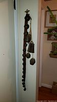Full view of cowbells and sleighbells hanging on a red vertical strap against a wall